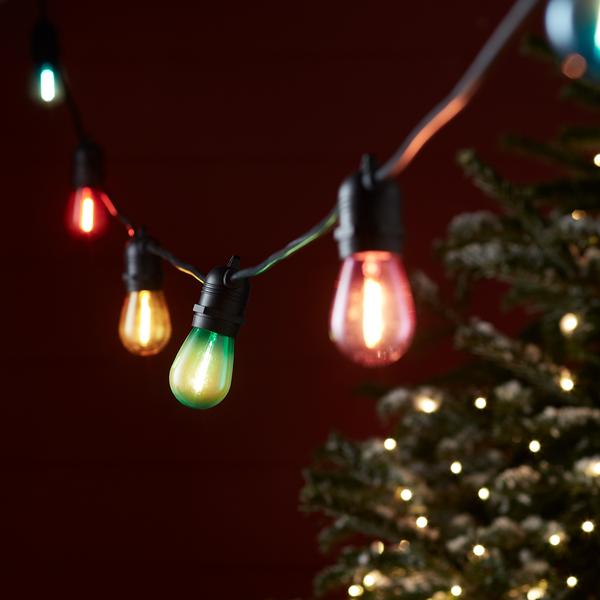 Bunte LED-Glühbirnenkette vor rotem Hintergrund und Weihnachtsbaum