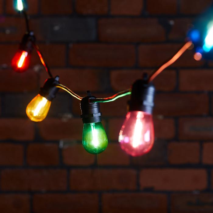 Bunte LED-Glühbirnen an schwarzem Kabel vor Ziegelwand, rot, grün, gelb leuchtend