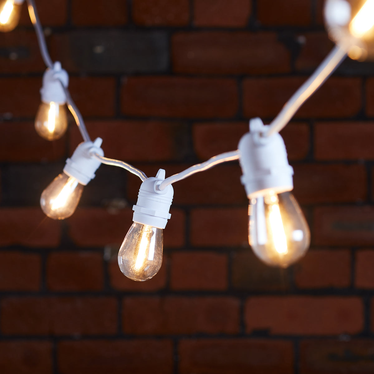Warmweiße Glühbirnen an weißem Kabel vor dunkler Backsteinwand