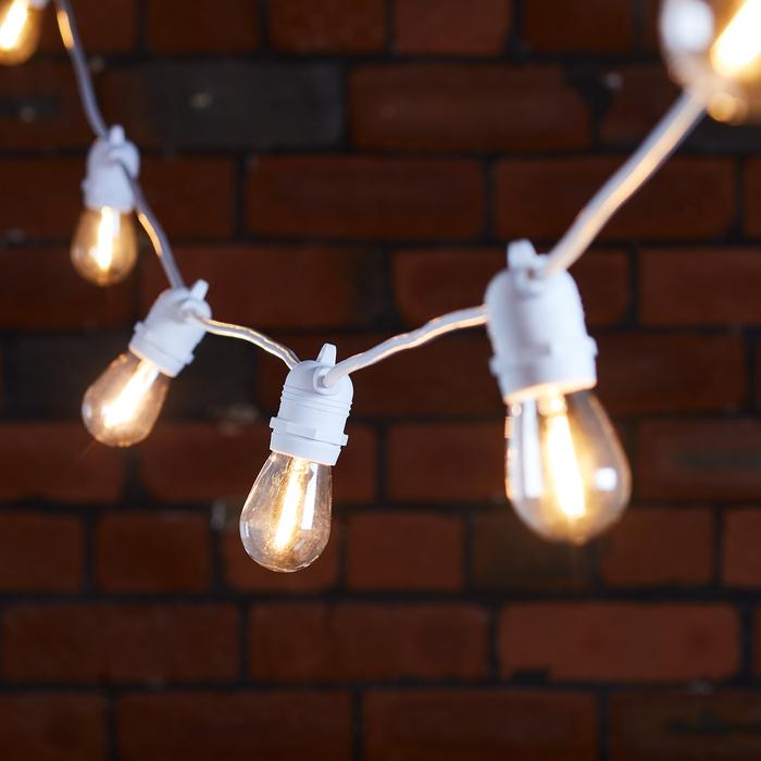 Warmweiße Glühbirnen an weißem Kabel vor dunkler Backsteinwand
