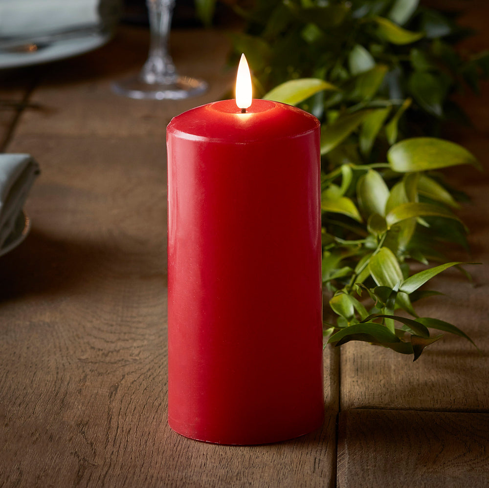 Rote LED Echtwachs-Kerze mit Flamme auf Holztisch neben grünen Blättern