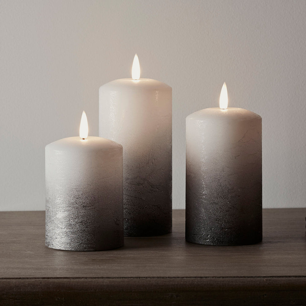 Trio grauer Ombré LED-Kerzen mit flackernder Flamme vor weißer Wand auf dunklem Untergrund