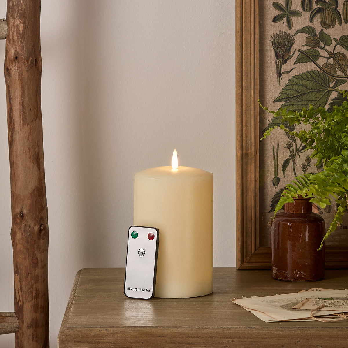Große LED Stumpenkerze mit Fernbedienung auf Holzfläche neben Glasvase und Büchern