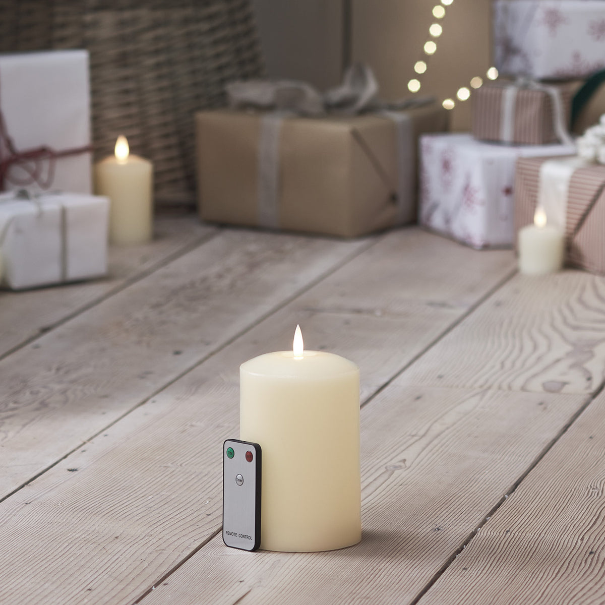 LED Stumpenkerze mit Fernbedienung auf hellem Holzboden vor Weihnachtsgeschenken