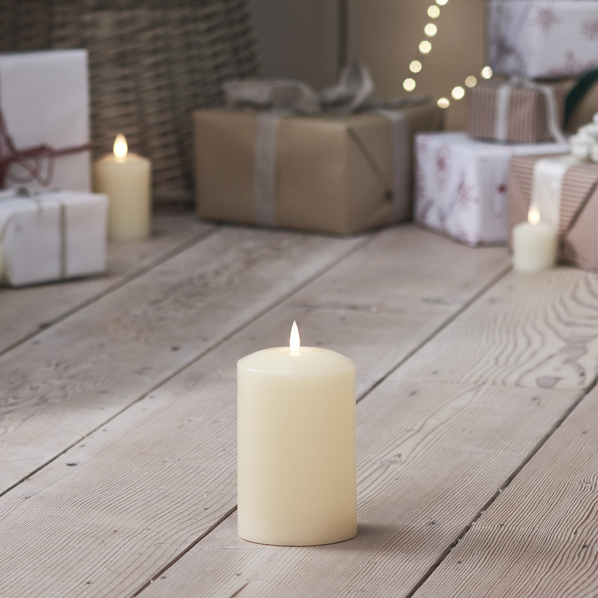 LED Stumpenkerze auf hellem Holzboden vor Geschenken und Laterne mit warmem Licht