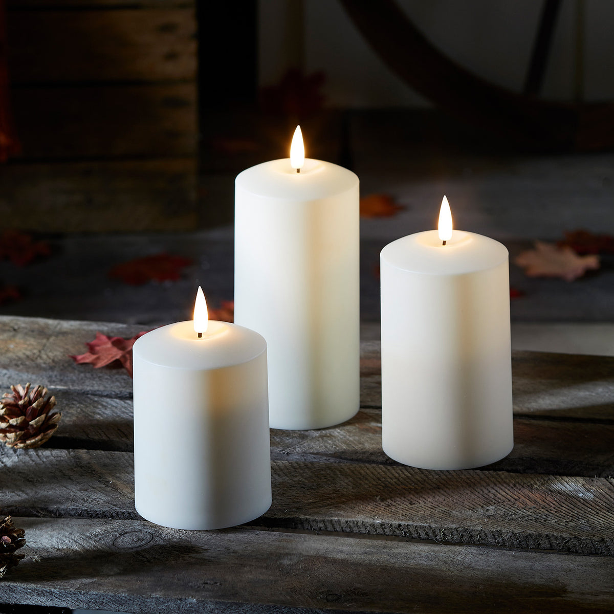 Drei TruGlow LED Kerzen mit Flamme auf rustikalem Holztisch bei gedimmtem Licht