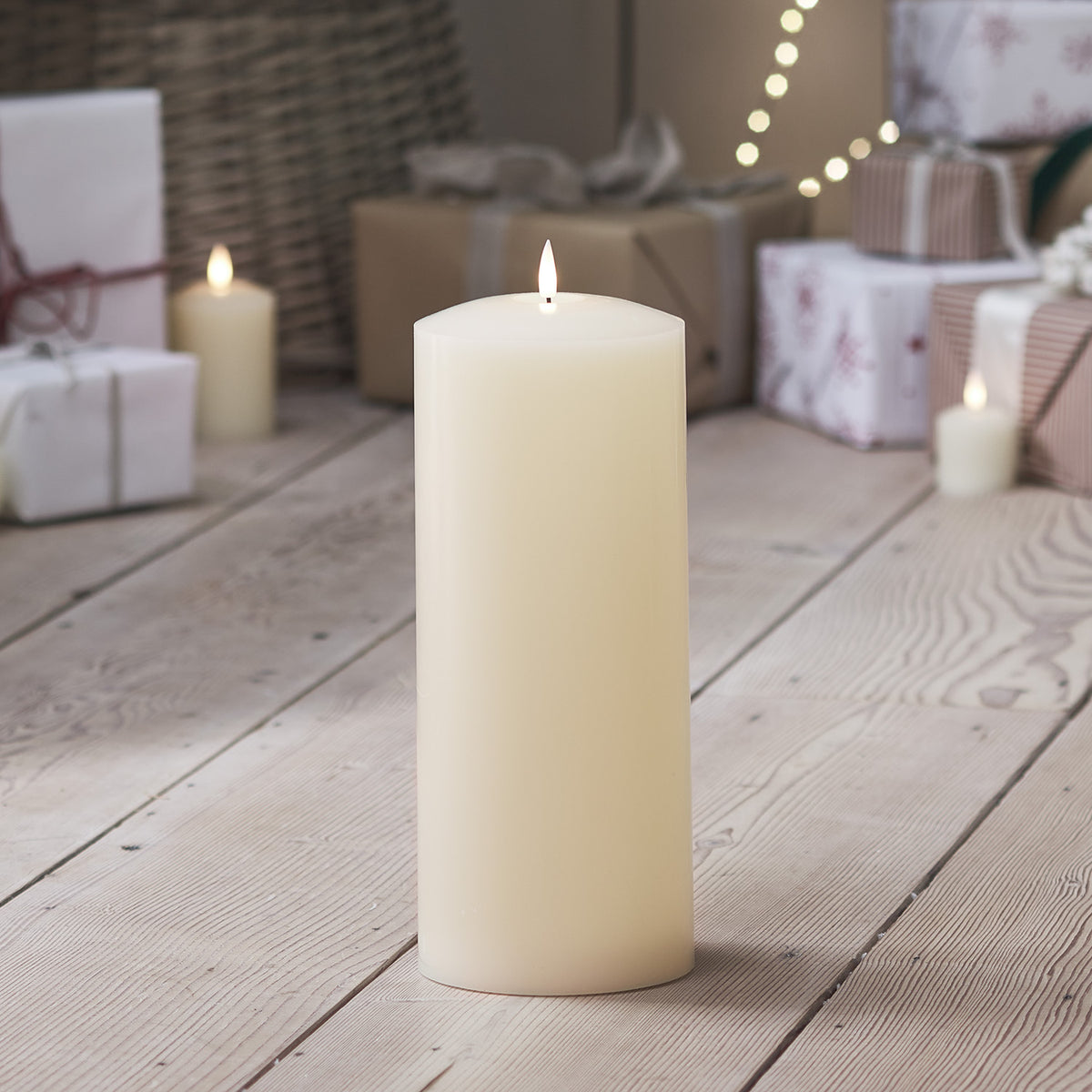 LED Stumpenkerze auf Holzboden mit Weihnachtsgeschenken und weiteren Kerzen im Hintergrund
