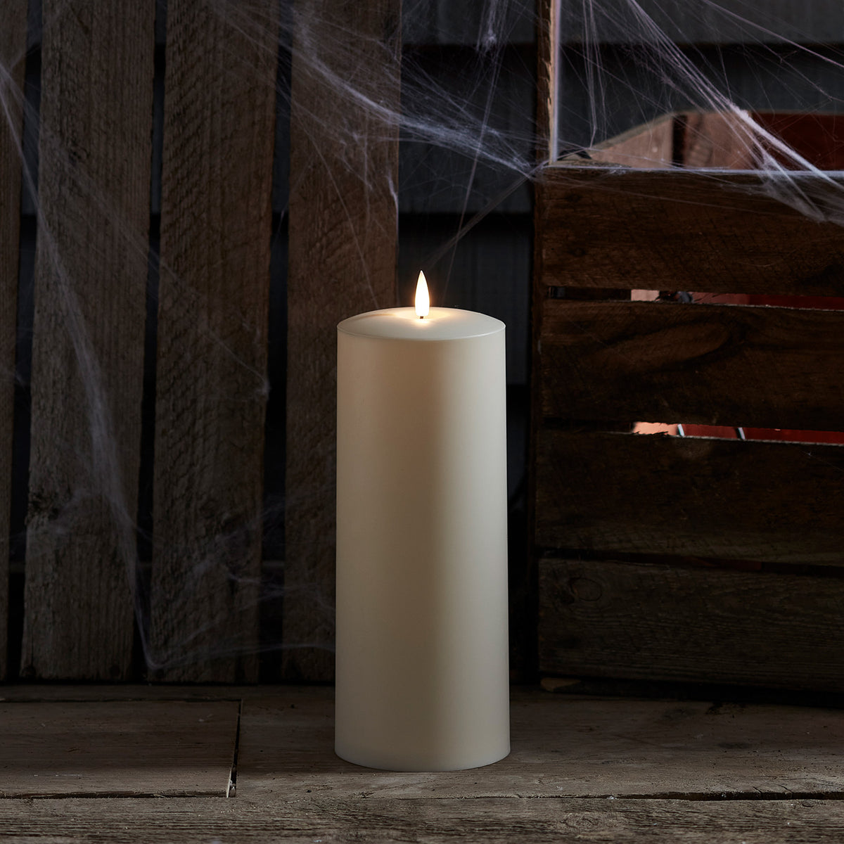 TruGlow LED Outdoor Kerze mit Flamme vor Holzkiste und Spinnweben als Dekoration