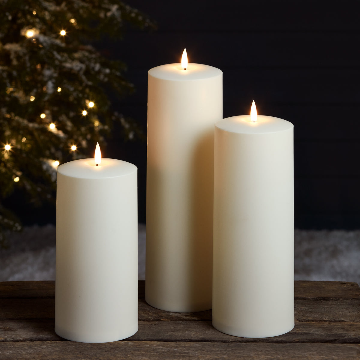 Drei weiße LED Kerzen vor dunklem Hintergrund mit Weihnachtsbaumbeleuchtung