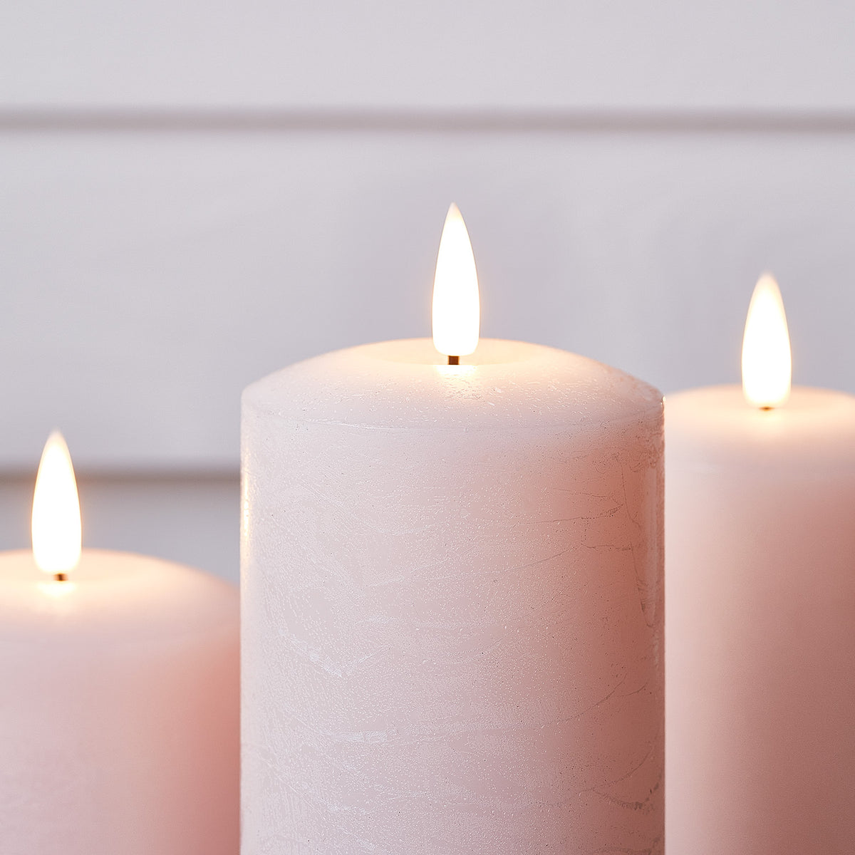 Drei rosa LED Stumpenkerzen mit Fernbedienung auf Tisch mit Osterdeko und Blumen