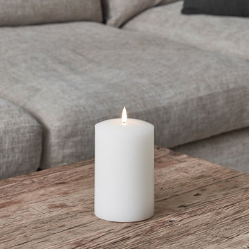 Weiße breite LED Stumpenkerze aus Echtwachs auf Holztisch vor grauem Sofa