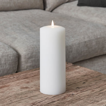 Weiße breite LED Stumpenkerze aus Echtwachs auf Holztisch vor grauem Sofa