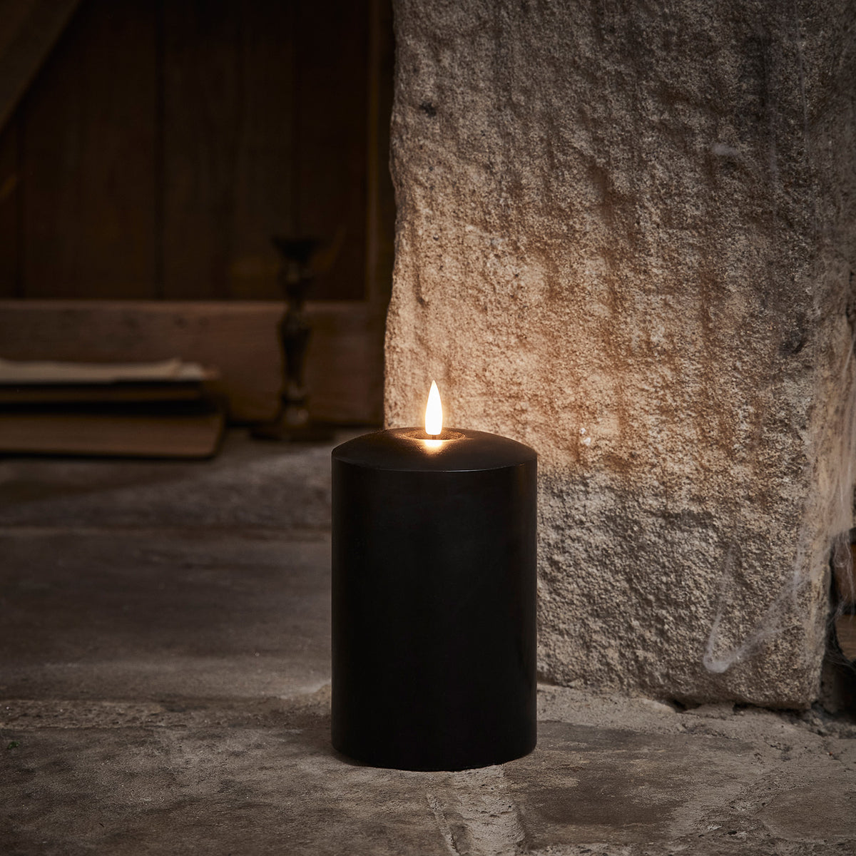 Schwarze breite LED Stumpenkerze aus Echtwachs mit flackernder Flamme vor Steinwand