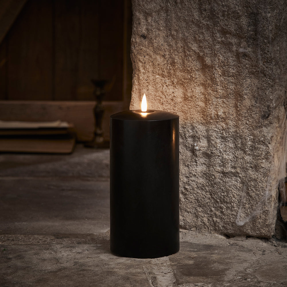 Schwarze breite LED Stumpenkerze aus Echtwachs mit flackernder Flamme vor Steinwand