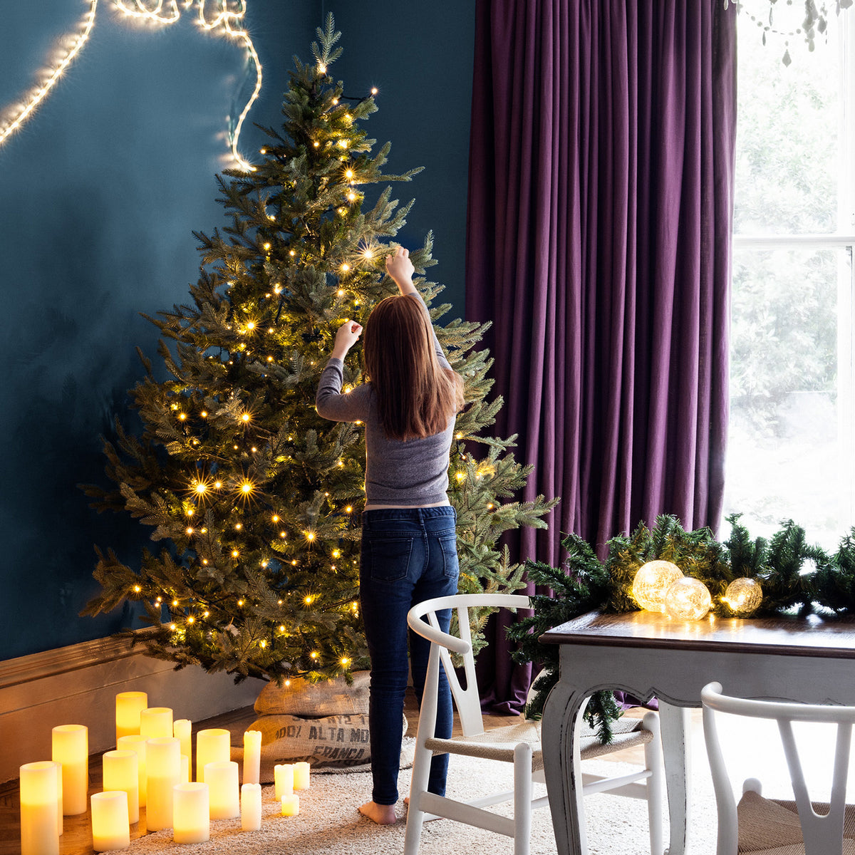 Frau schmückt Weihnachtsbaum mit warmweißer LED-Lichterkette in einem Wohnzimmer