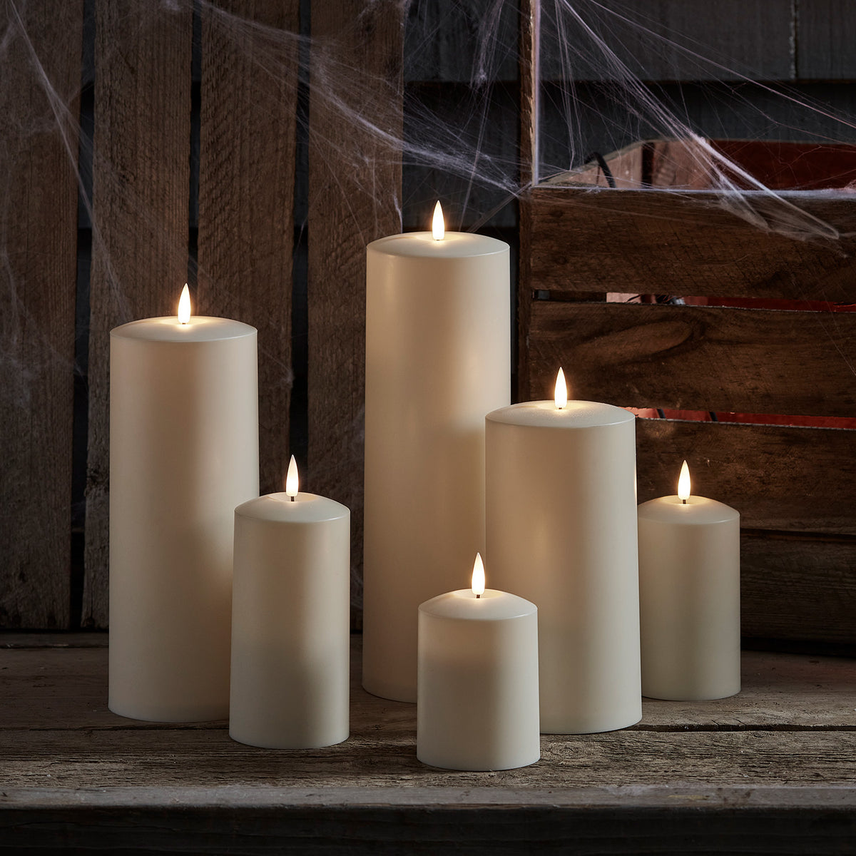 Sechs brennende TruGlow LED Outdoor Kerzen vor Holzkiste mit Spinnweben