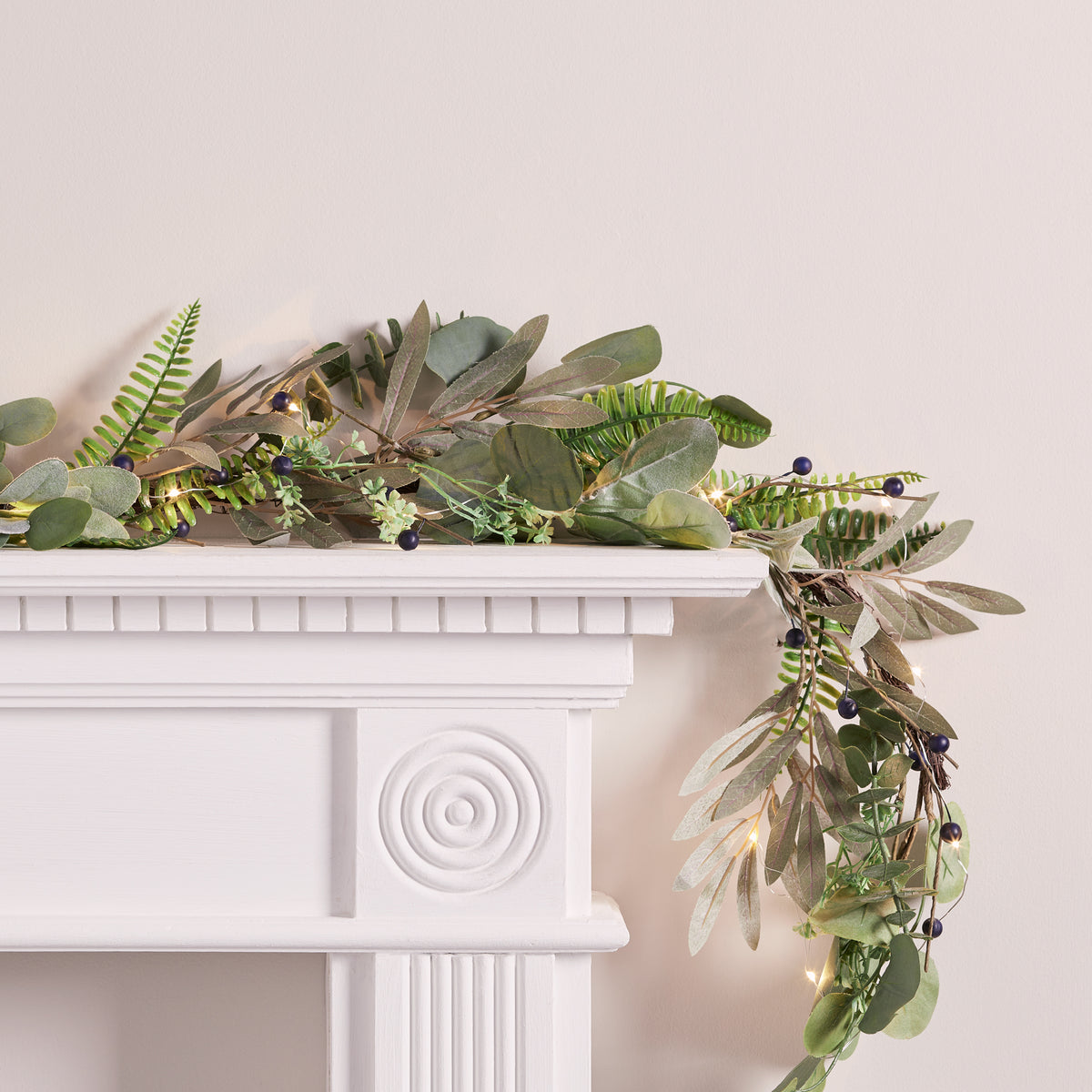 Weihnachtsgirlande mit grünen Blättern, blauen Beeren und Micro Lichterkette auf weißem Kaminsims