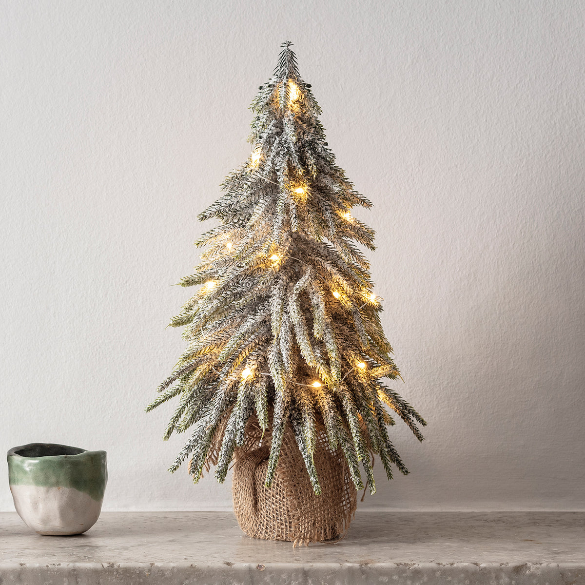 Nahaufnahme eines 35cm Mini Weihnachtsbaums mit Schnee und warmweißer Micro Lichterkette auf Marmorfläche