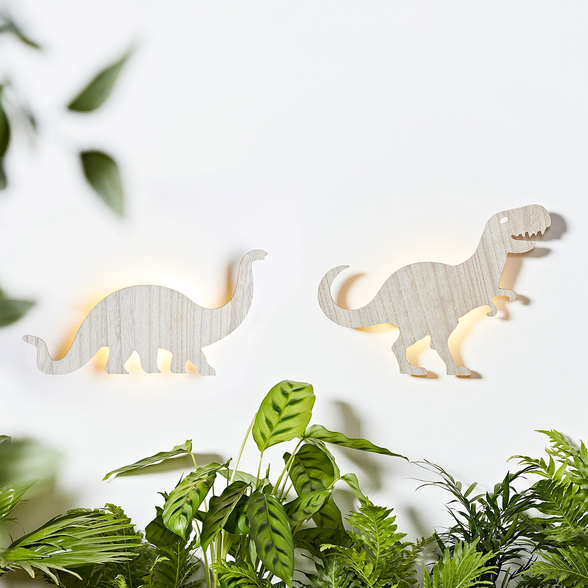 Zwei beleuchtete Holz Wandlampen in Dinosaurierformen Diplodocus und T-Rex an weißer Wand