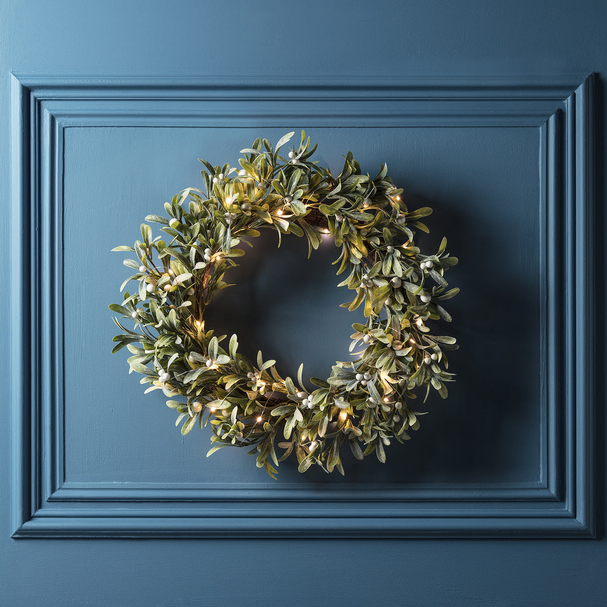 Mistelzweig Weihnachtskranz mit weißen Perlen und Micro Lichterkette an blauer Wand