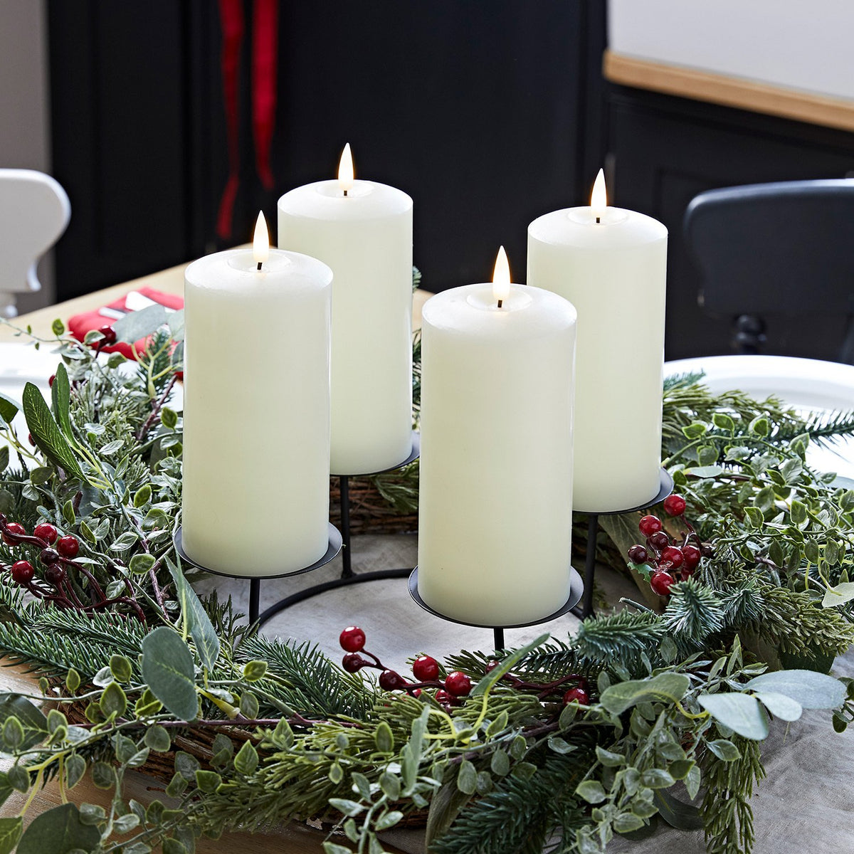 Adventskranz mit grünen Zweigen, roten Beeren und vier weißen LED-Kerzen auf schwarzem Metallständer