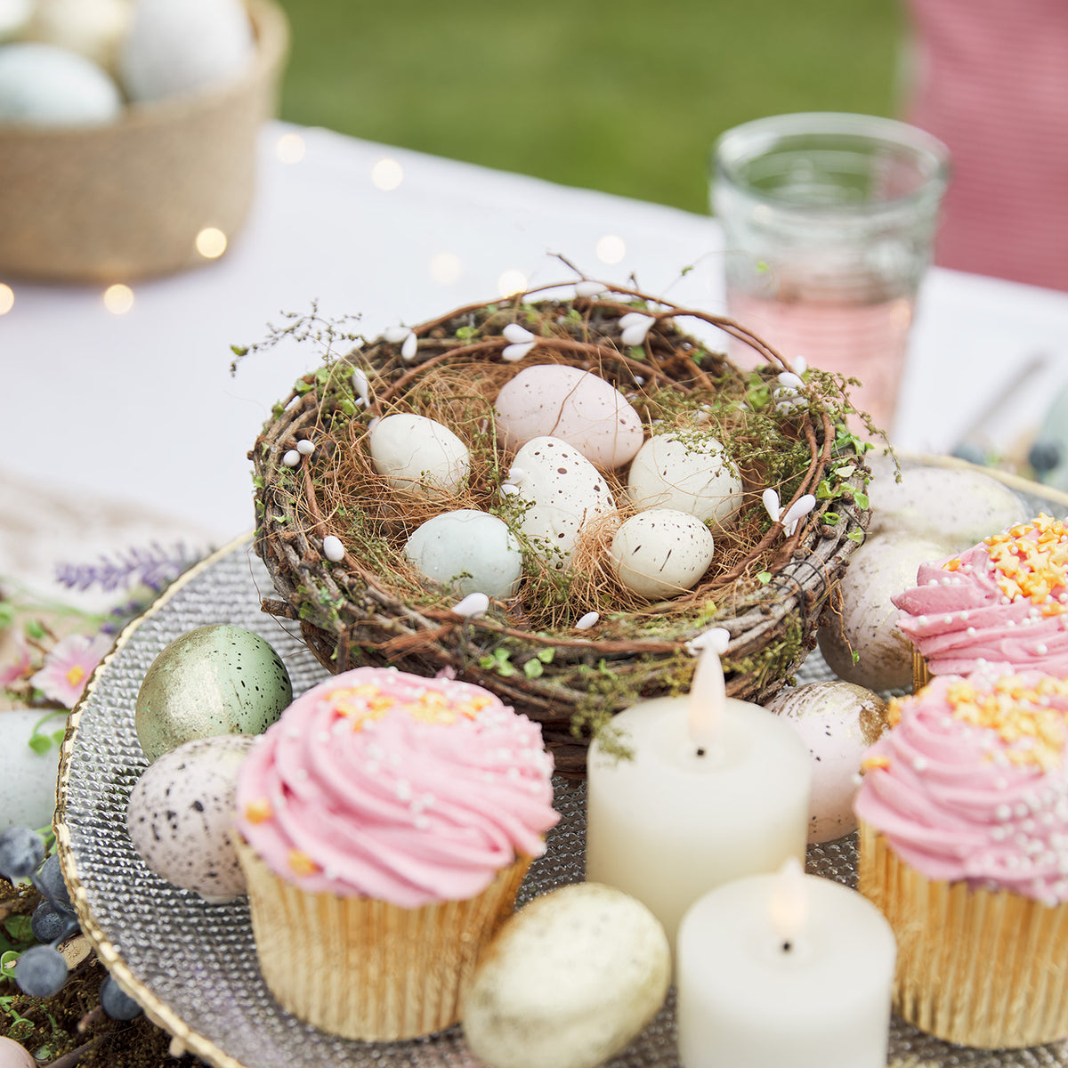 Osternest mit Eiern auf einem Tisch mit rosa Cupcakes und weißen Kerzen dekoriert