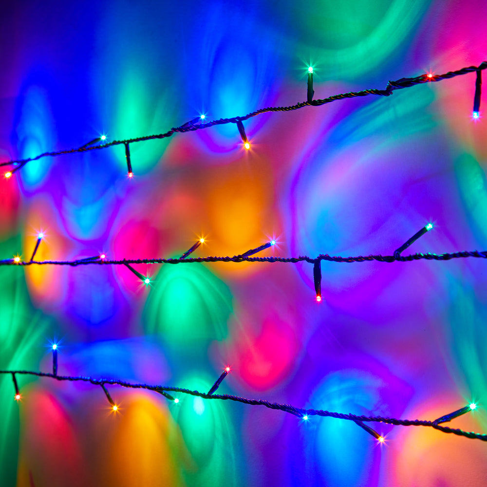 Bunte LED-Lichterkette mit grünem Kabel vor farbig beleuchteter Wand