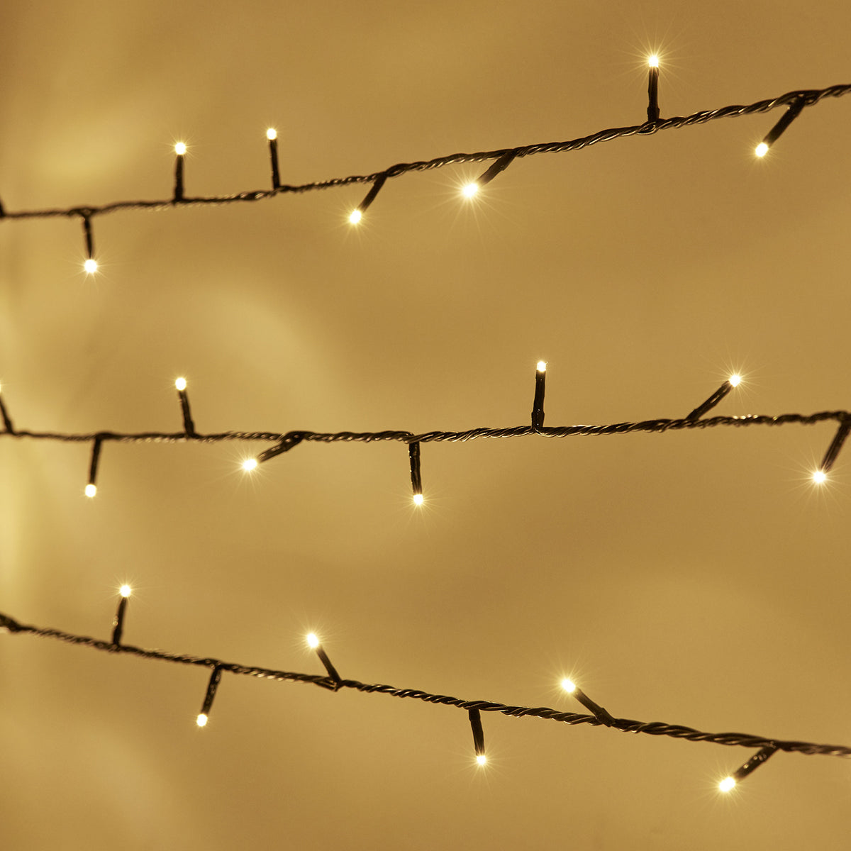 Nahaufnahme warmweiße LED-Lichterkette mit grünem Kabel vor beige Hintergrund