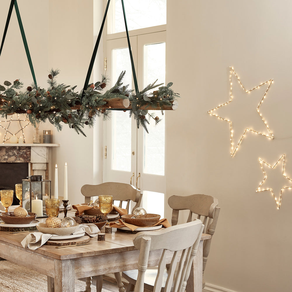 Esszimmer mit festlich gedecktem Holztisch und zwei leuchtenden goldenen Sternen an der Wand