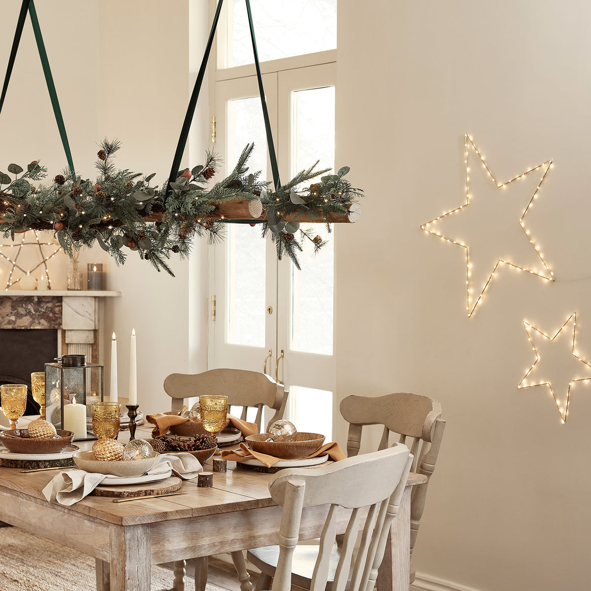 Esszimmer mit festlich gedecktem Holztisch und zwei leuchtenden goldenen Sternen an der Wand