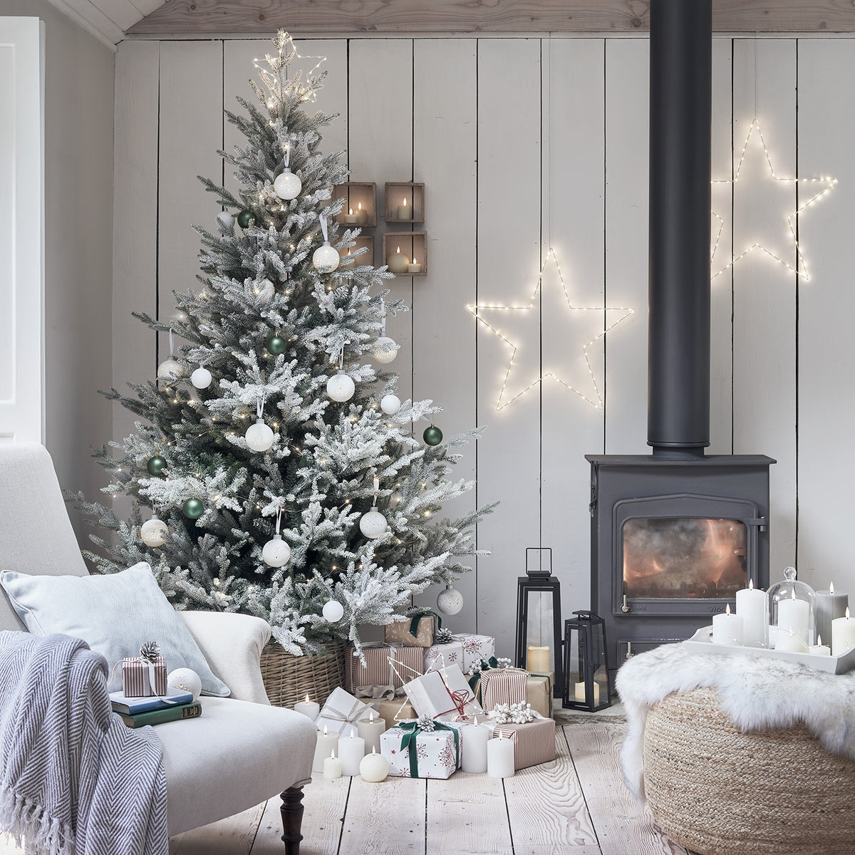 Großer und kleiner leuchtender weißer LED-Stern mit warmweißen LEDs an Wand neben Weihnachtsbaum und Kamin
