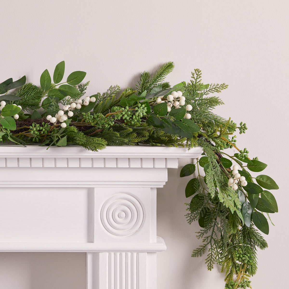 Weihnachtsgirlande mit grünen Blättern und weißen Beeren auf weißem Kaminsims