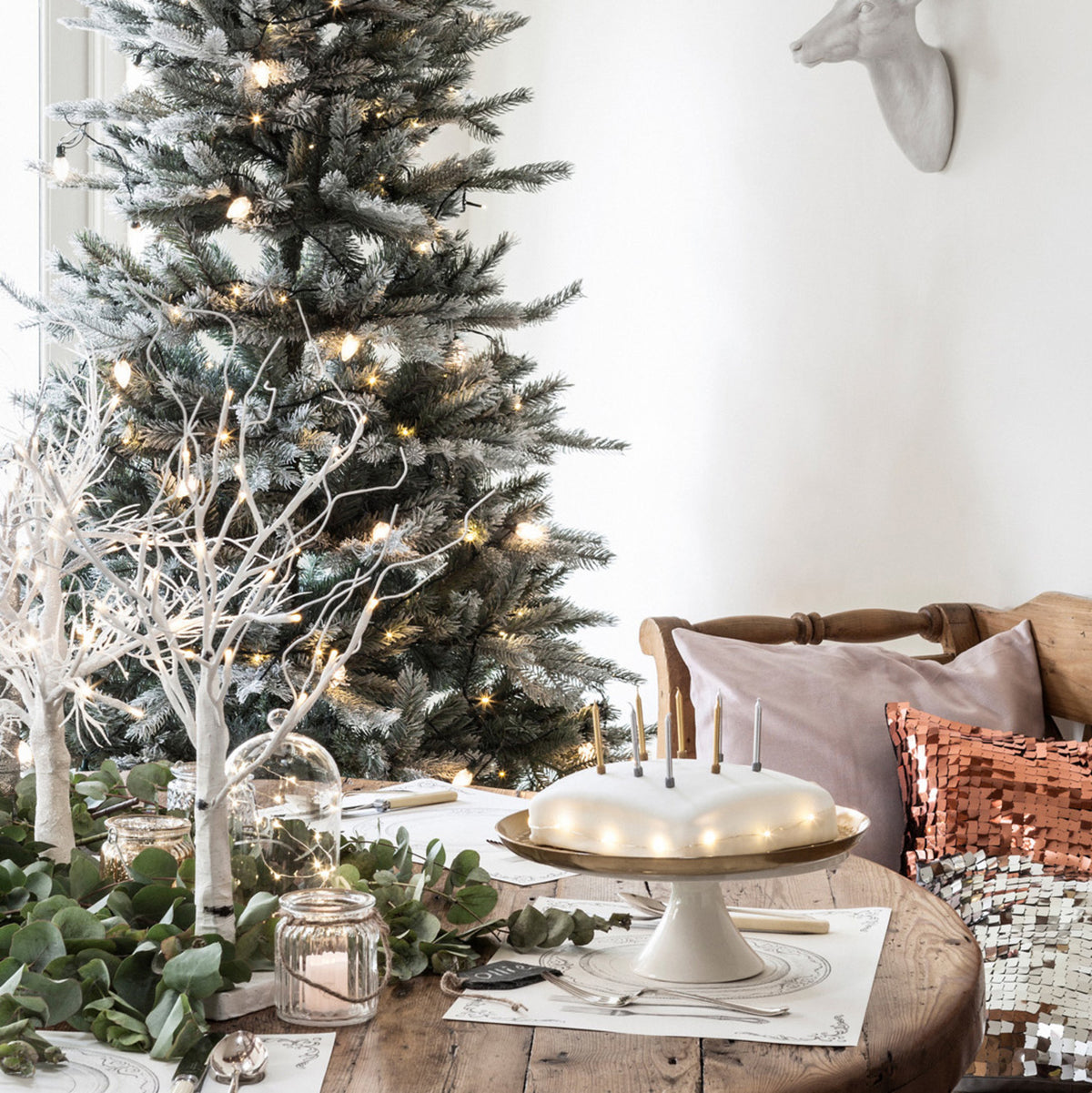 Weihnachtlich dekorierter Tisch mit Glasglocke, Kerzen, Eukalyptuszweigen und beleuchtetem Weihnachtsbaum