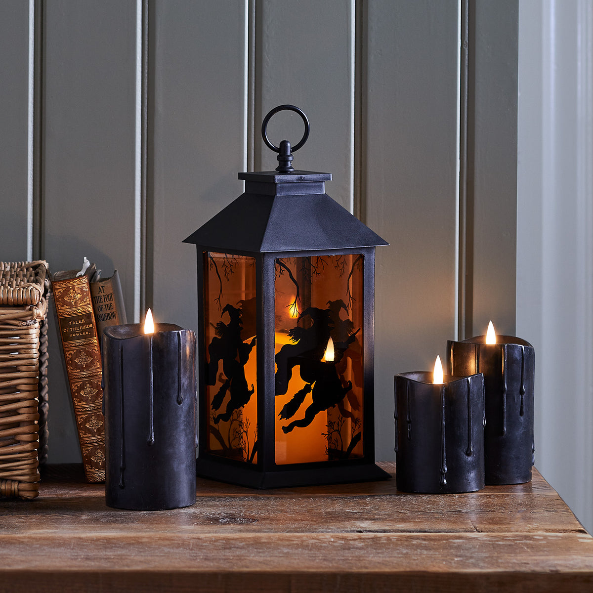 Schwarze LED Kerzen neben einer Halloween-Laterne mit Hexen-Motiv auf Holztisch