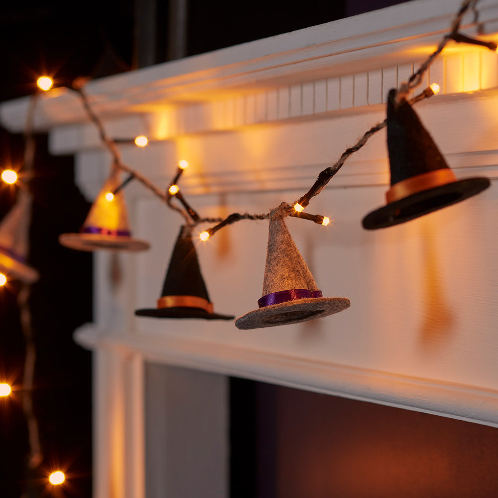 Halloween Lichterkette mit Filz-Hexenhüten in Schwarz und Grau, beleuchtet am Kaminsims