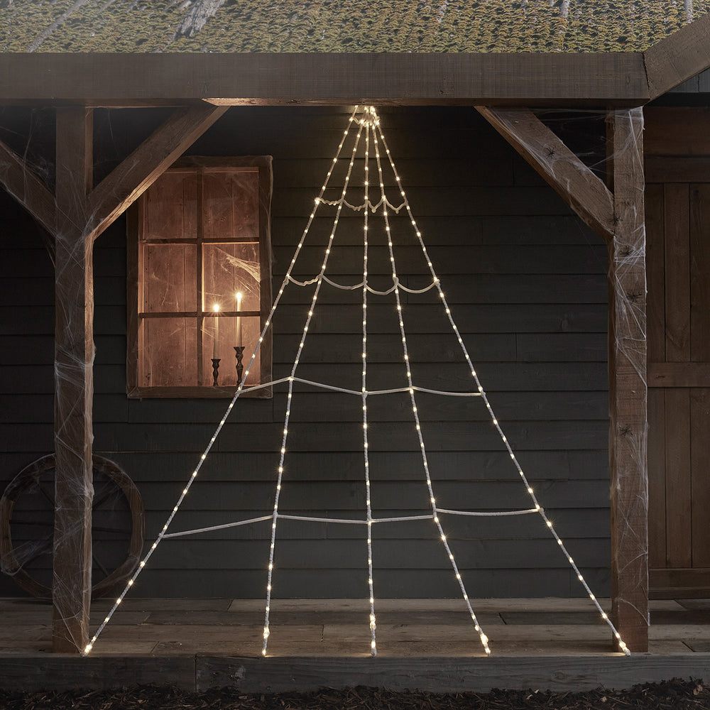 Leuchtendes Halloween Spinnennetz mit warmweißen LEDs an dunkler Wand im Außenbereich