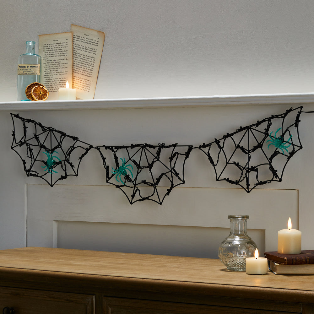 Nahaufnahme der Halloween Lichterkette mit drei Spinnennetzen und grünen Spinnen über einem Kamin