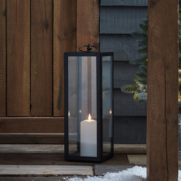 Große schwarze Gartenlaterne mit TruGlow Outdoor Kerze vor Holzwand und Schnee