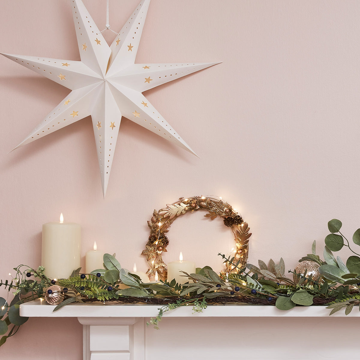 Großer weißer Papierstern mit LED-Beleuchtung hängt über einem Kamin mit Kerzen, Kranz und grüner Deko
