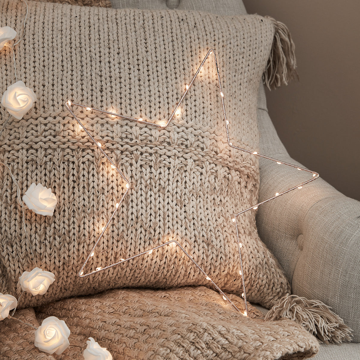 Leuchtender LED-Stern in Roségold auf grob gestricktem Kissen auf Sessel mit Lichterkette