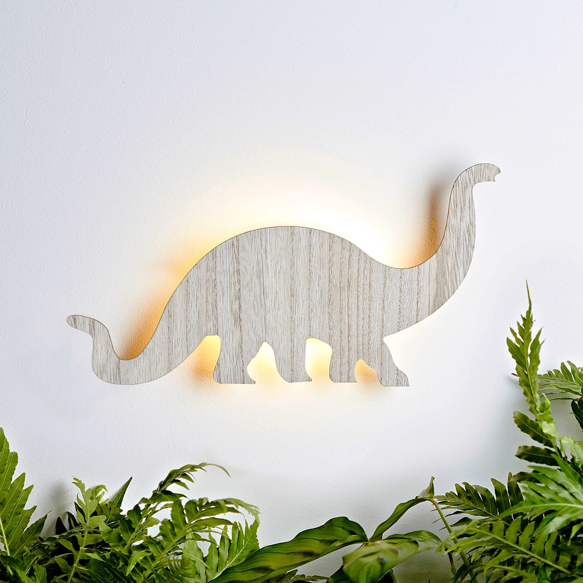 Holz-Wandlampe in Form eines langhalsigen Diplodocus mit warmem Licht an weißer Wand