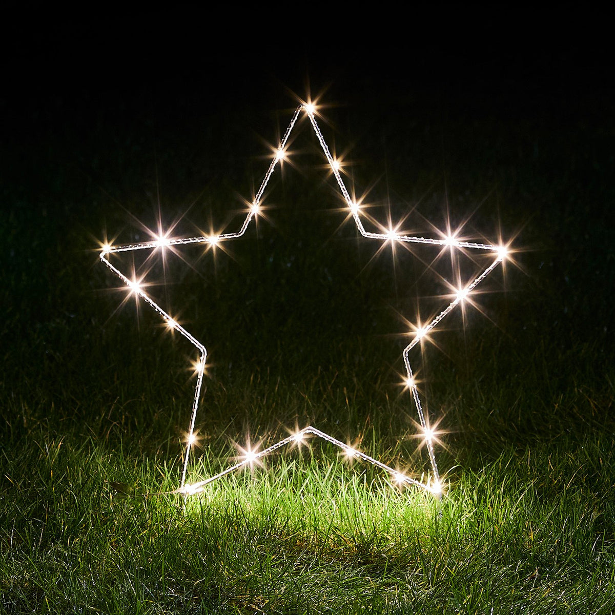 Ein einzelner beleuchteter Stern aus Micro LED-Lichtern auf grünem Gras bei Nacht