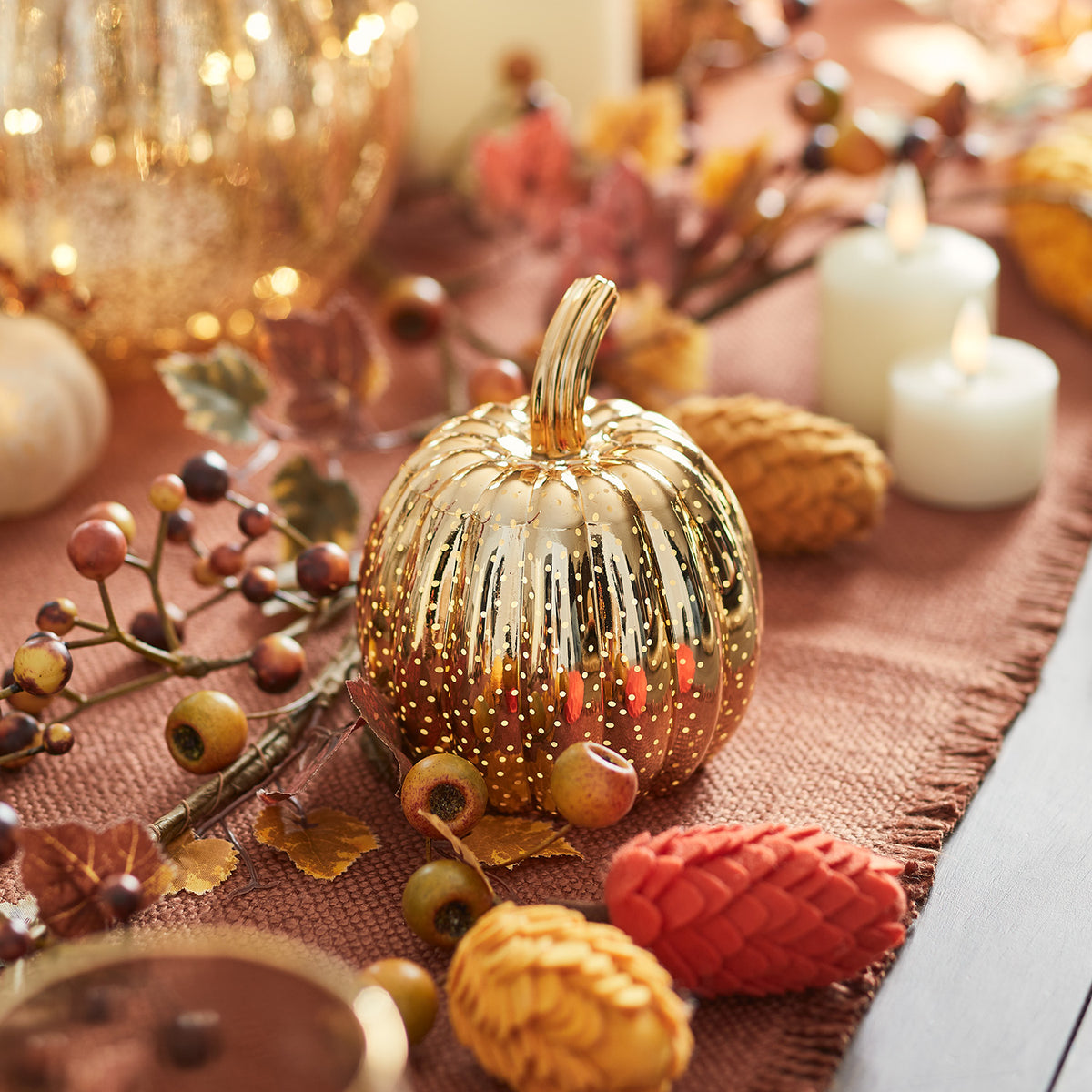 Mini-LED-Kürbis aus Glas mit Herbstdeko und Kerzen auf orangefarbenem Stoff