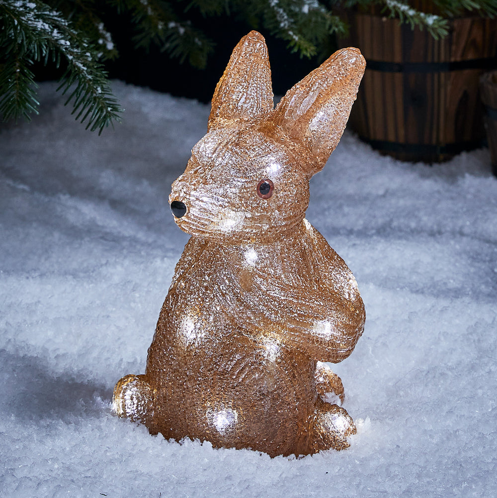 Leuchtende LED Acrylfigur eines Hasen im Schnee vor Tannenzweigen bei Nacht