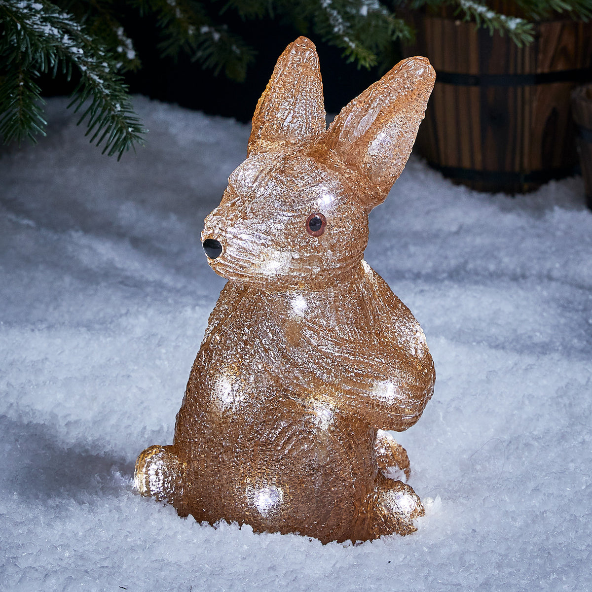 Leuchtende LED Acrylfigur eines Hasen im Schnee vor Tannenzweigen bei Nacht