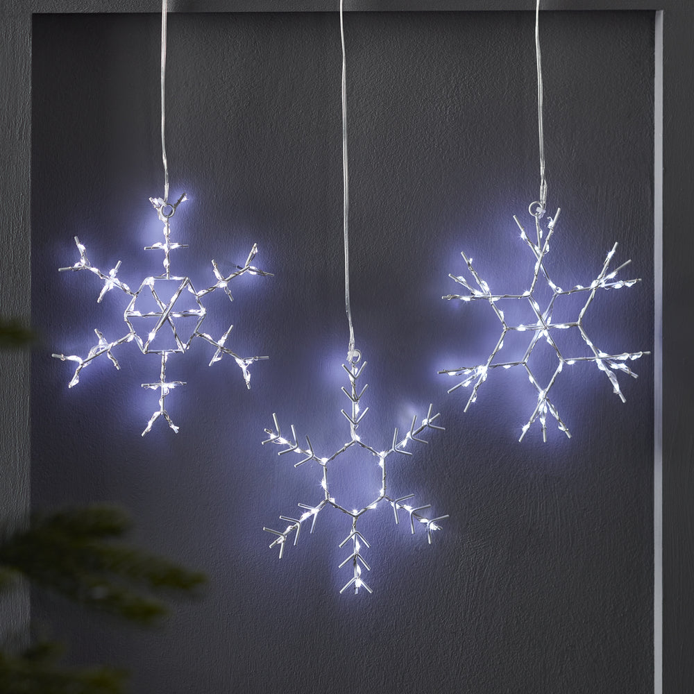 Drei leuchtende LED-Schneeflocken aus Metall vor dunkler Wand hängend