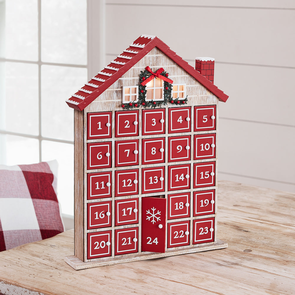 Holz-Adventskalender in Form eines Bauernhauses mit roten Türen und weißen Zahlen auf Holztisch