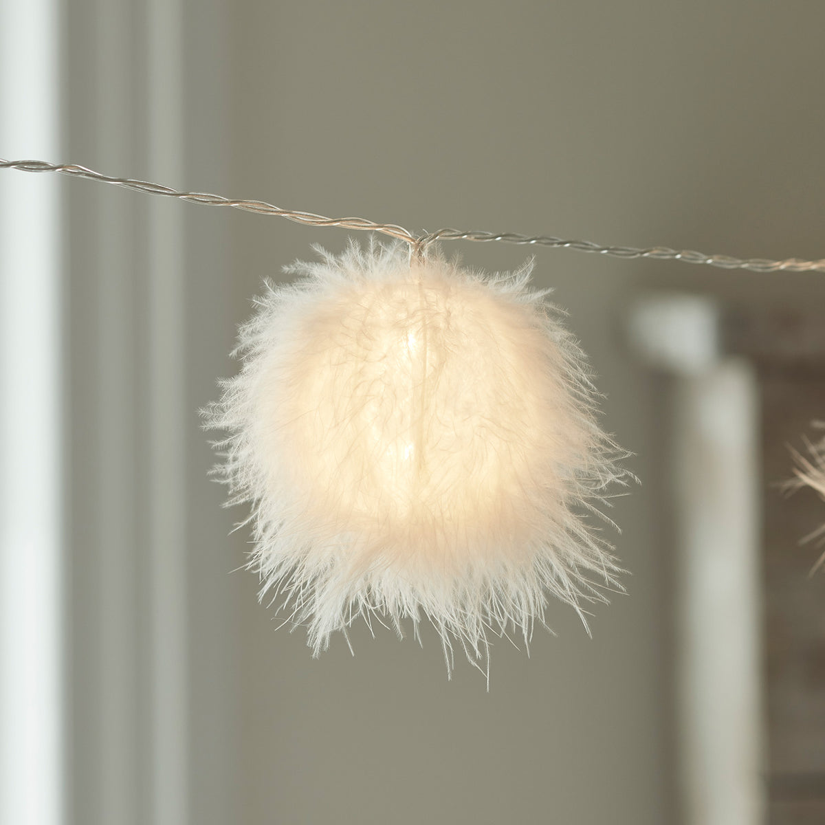 Detailaufnahme eines leuchtenden, flauschigen weißen Balls an einer Lichterkette