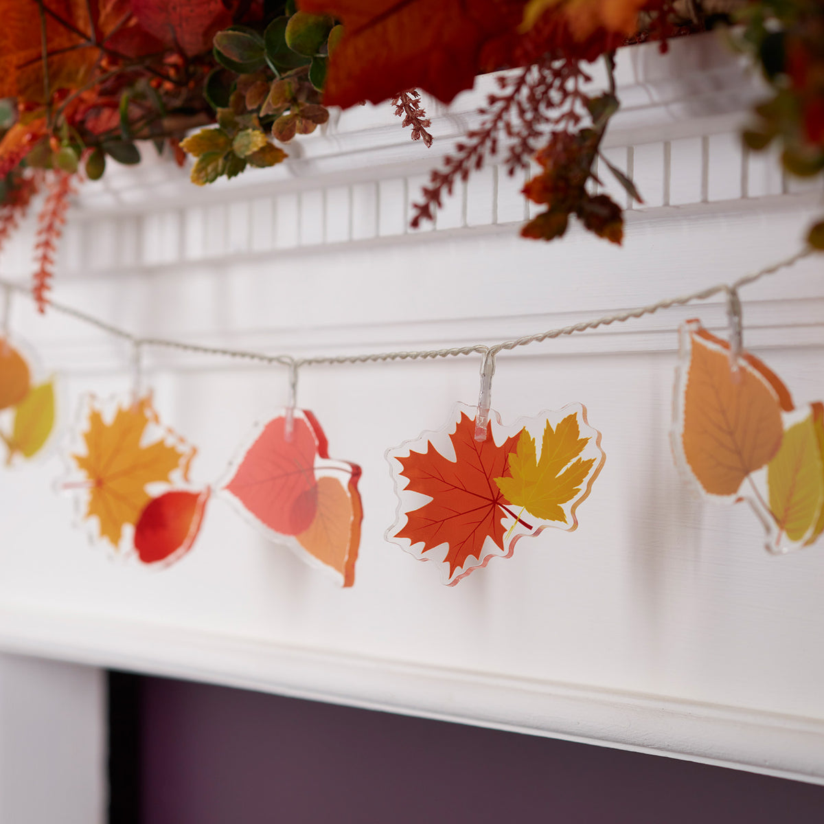 Lichterkette mit Acryl-Ahornblättern in Herbstfarben ohne Beleuchtung an weißem Kaminsims