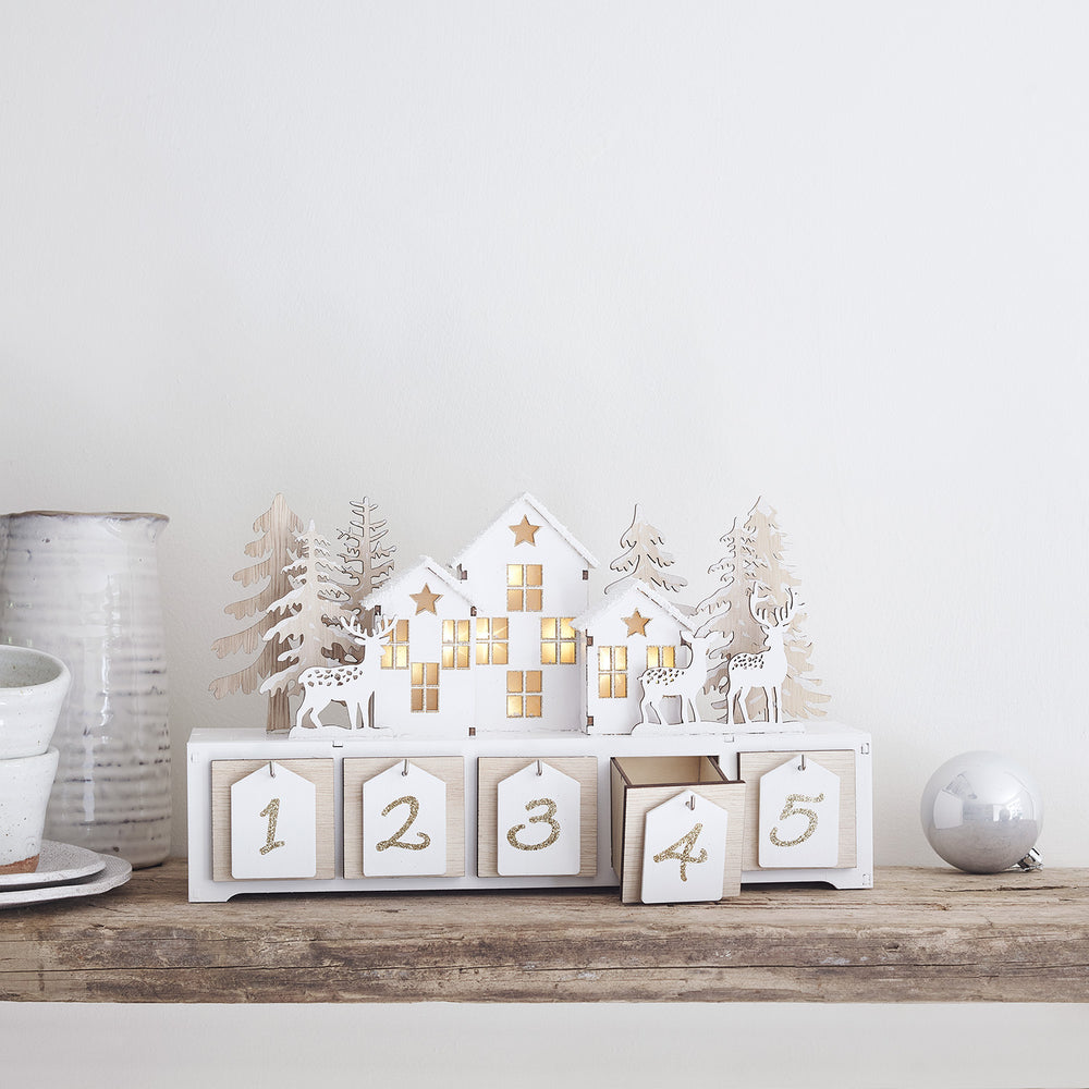 Holzadventskalender mit beleuchteten Häusern, Rentieren und Tannenbäumen auf Holzablage